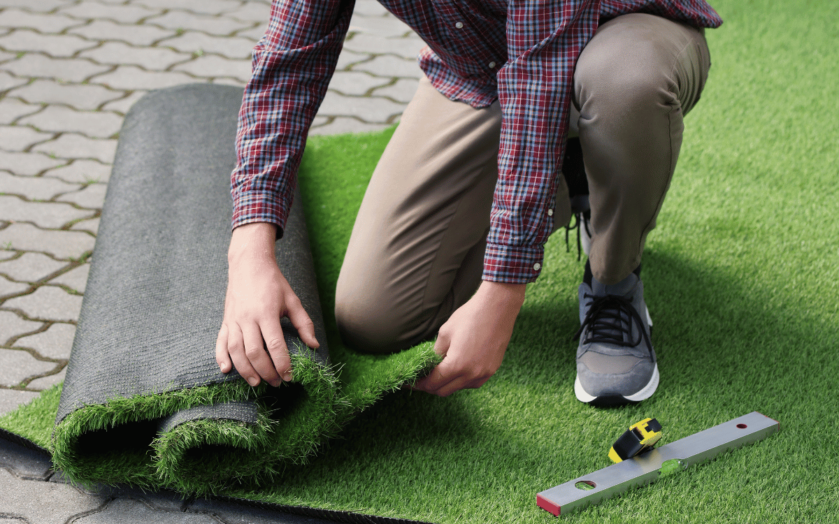Profesional instalando césped artificial en jardín con herramientas de precisión